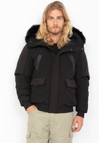Schwarze gepolsterte Jacke mit einer Kapuze aus Kunstfell, Reißverschlusstaschen und Druckknöpfen. Sie hat eine glatte Stoffoberfläche und einen strukturierten Schnitt.