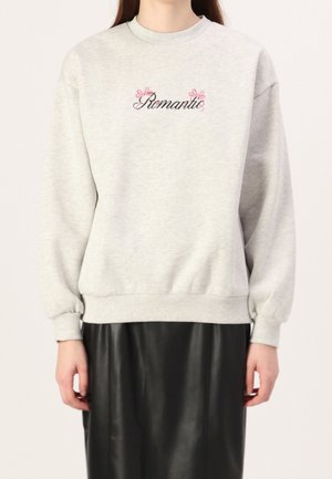 Grauer Pullover mit gesticktem "Romantic"-Text und Blumenakzenten, mit Rundhalsausschnitt und elastischen Bündchen, über einem schwarzen Rock getragen.