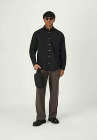 Camicia nera con bottoni, pantaloni marroni a gamba larga, occhiali da sole neri e una piccola borsa a tracolla nera. Tessuto liscio con vestibilità comoda.