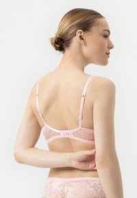 Kanten bralette in zachtroze, met verstelbare bandjes, een haak-en-oogsluiting en ingewikkelde bloemenpatronen langs de band.