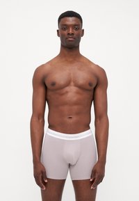 Graue Boxershorts mit einem weißen Calvin Klein Logo am Bund, aus einem glatten, dehnbaren Material, enganliegendem Schnitt und einer Länge bis zur Mitte des Oberschenkels.