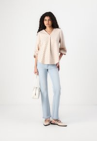 Blusa rosa chiaro a fantasia con maniche a sbuffo, abbinata a jeans flared azzurri e ballerine beige. Gli accessori includono una piccola borsa bianca.