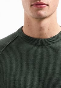 Groene gebreide trui met een gestructureerd, geribbeld ontwerp en een ronde halslijn, met subtiele stikdetails op de schouders.