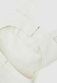 Valkoinen kangasasu, jossa leveät olkaimet, sileä pinta ja sivuvetoketjukiinnitys. Malli on selkeä ja minimalistinen.