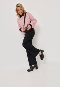 Roza volnena blenda pričeska z črnimi manšetami, črnimi širokimi hlačami in črnimi čevlji s peto. Nošena je majhna črna torbica preko telesa.