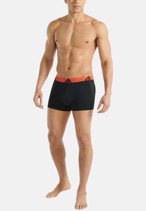 Zwarte boxershorts met een oranje elastische tailleband, voorzien van een logo en drie zwarte strepen, ontworpen voor comfort en ondersteuning.