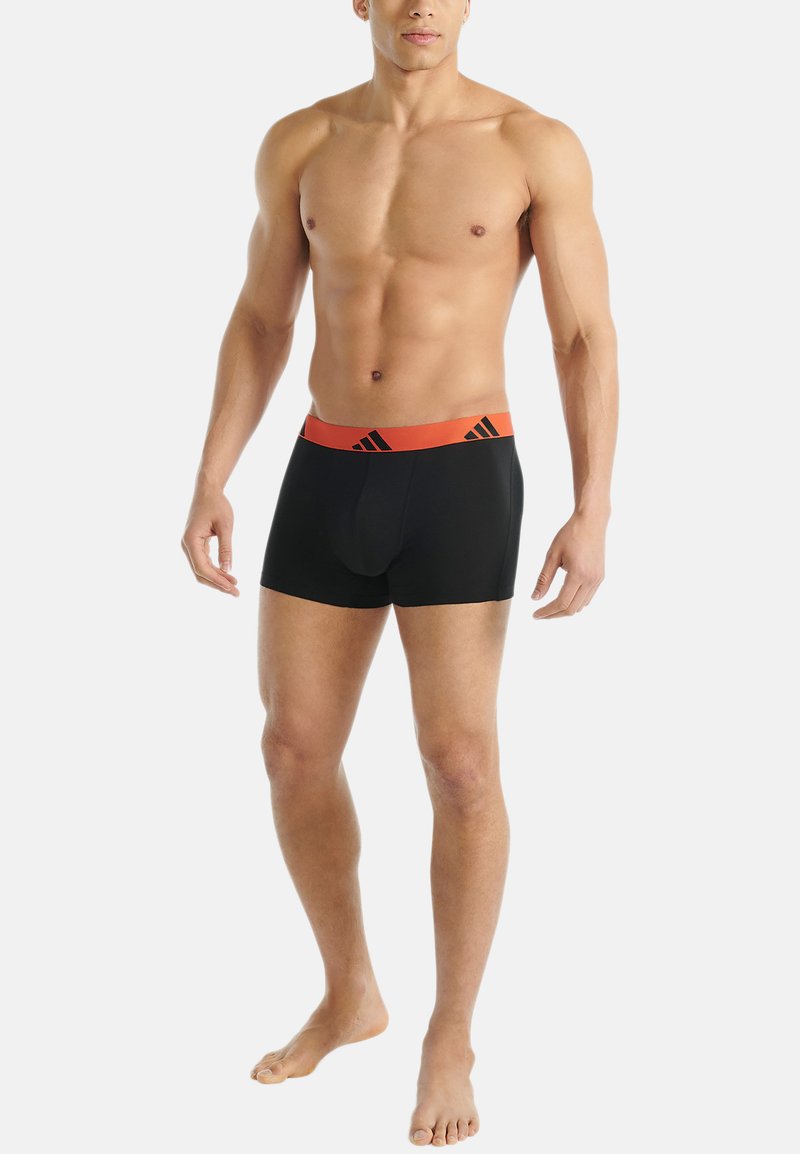 Zwarte boxershorts met een oranje elastische tailleband, voorzien van een logo en drie zwarte strepen, ontworpen voor comfort en ondersteuning.