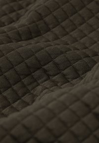 Gros plan sur un tissu sombre avec un motif matelassé texturé en grille, présentant des sections carrées en relief et des lignes cousues.