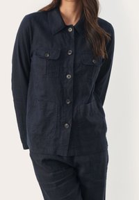 Chaqueta de lino azul marino con cuello, seis botones en la parte delantera y dos bolsillos en el pecho. Presenta una textura suave y un corte relajado con mangas largas.