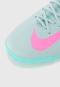 Nike sports shoe featuring a light blue synthetic upper, pink swoosh logo, and aqua outsole; textured surface with prominent lacing.