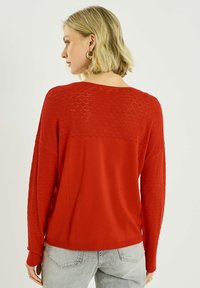 Suéter rojo con patrón de diamantes texturizados en las mangas y la espalda, con cuello redondo y ajuste relajado. Material suave.