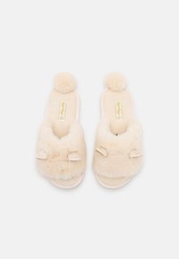 Light beige fluffy slippers with pom-poms on the upper, featuring a slip-on design and soft fabric texture. Accents include decorative ears.