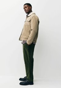 Beige suede jacket with a fur collar, black and white checkered shirt underneath, green corduroy pants, and black boots.
