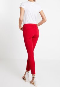 Röda slim fit-jeans med en slät yta, bakfickor och en figurnära design, kombinerat med en enkel vit t-shirt och vita högklackade sandaler.