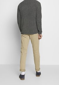 Szary sweter dziany, beżowe chino oraz niebieskie zamszowe buty. Sweter ma fakturowany wzór i długie rękawy. Chino są podwinięte przy mankietach.