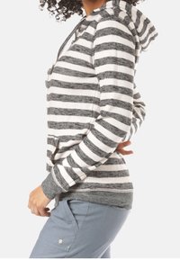 Sudadera a rayas grises y blancas con un bolsillo frontal, puños grises y capucha con cordón. La tela parece suave con un acabado texturizado.