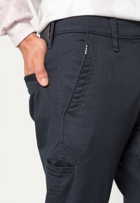 Navy blue cargo pants with a smooth, textured finish, featuring slanted front pockets and a stitched logo on the waistband.