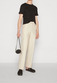 Sort ribbet t-shirt med kortærmer og øjenlåg detaljer, parret med lysebeige brede bukser og en sort rund crossover taske. Sorte kanvas sko.