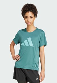 Tyrkysové sportovní tričko s krátkými rukávy, s velkým světle modrým logem Adidas. Lehký, materiál odvádějící vlhkost, hladká textura.