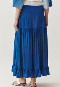 Blauwe maxi rok met lagen en een smock tailleband en flonkerzoom. Gemaakt van zacht materiaal, heeft het een gladde textuur en een vloeiende stijl.