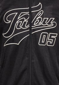 Sort lynlåsjakke med hvid broderet tekst "Fubu" og "05" på fronten. Glat tekstur med en subtil glans og lodret mønster.
