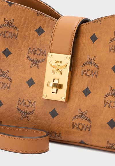 Sac en cuir marron MCM avec motifs losanges noirs et logo, fermeture à pince dorée, avec une bandoulière en cuir assortie.