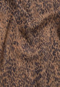 Tejido marrón con un estampado de leopardo en negro. La textura está ligeramente arrugada con secciones recogidas, creando una profundidad visual.