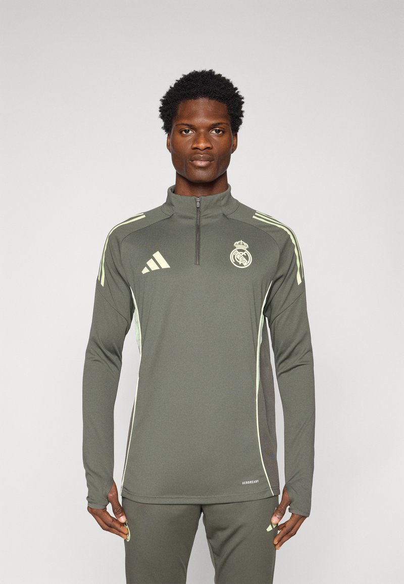 Dugi rukav sportski top u maslinastoj boji s četvrtim patent zatvaračem, kontrastnim svijetlozelenim bočnim panelima i logom Real Madrida na prsima.
