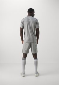 Sivý atletický dres s pohodlnými šortkami, má krátke rukávy a voľný strih. Biele akcenty a pruhované ponožky dopĺňajú celý outfit.