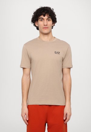 Camiseta de manga corta color marrón claro, hecha de una tela suave, con un pequeño logo negro de EA7 en el pecho. Diseño sencillo y de corte clásico.