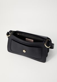 Black leather handbag with a structured design, featuring a zippered compartment, a front pocket with a gold button closure, and gold hardware accents.