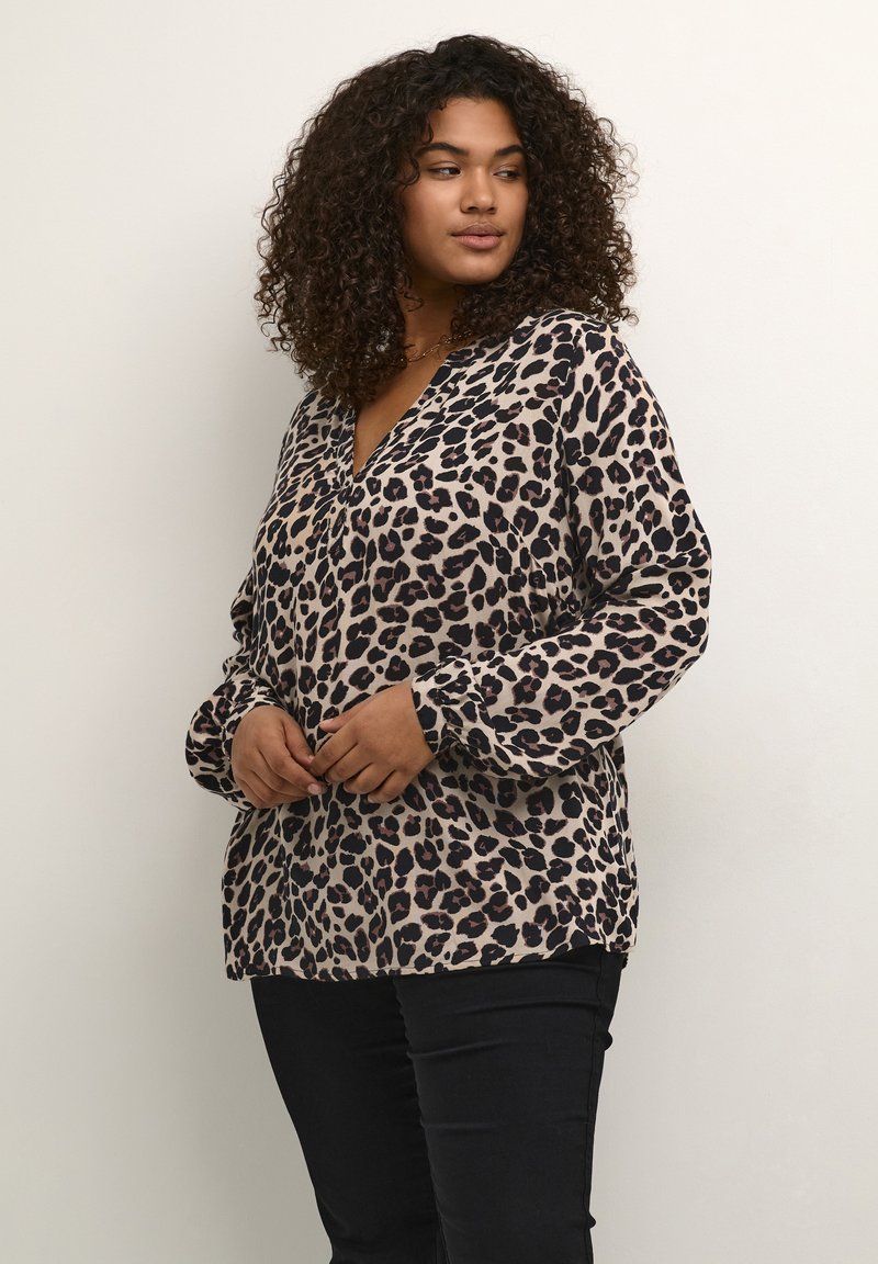 Blouse imprimée léopard en tissu doux, avec un décolleté en V et des manches longues. Accentuée de taches foncées sur un fond beige clair.