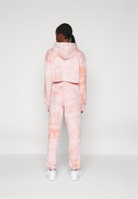 Rosa tie-dye cropped hettegenser og joggebukse-sett. Mykt stoff, avslappet passform, elastiske mansjetter og midjebånd. Kjennetegnet av fargegradientmønster.