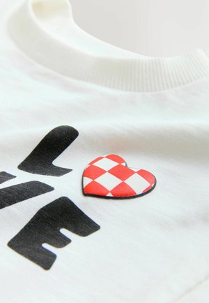 White cotton t-shirt featuring black printed letters and a red and white checkered heart-shaped patch on the front, round neckline.