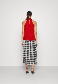 Rød halterneck-top med en nøglehul-detail, parret med en sort-hvid ternet nederdel med en flydende silhuet og ankelrem-sandaler.