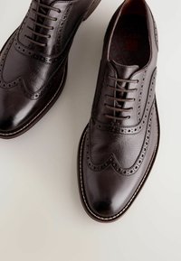 Chaussures habillées en cuir marron foncé avec un design lisse et texturé, ornées de brogue, à lacets fermés et avec une couture de semelle en contraste.