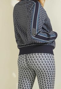 Giacca a tema navale con strisce blu, abbinata a leggings aderenti con un motivo logo grigio chiaro ripetuto.