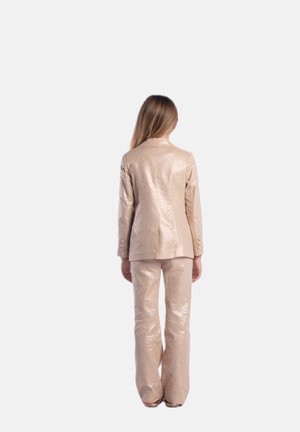Completo beige lucido a due pezzi con giacca aderente e pantaloni a zampa d'elefante. La giacca presenta quattro bottoni sui polsini e un design strutturato.