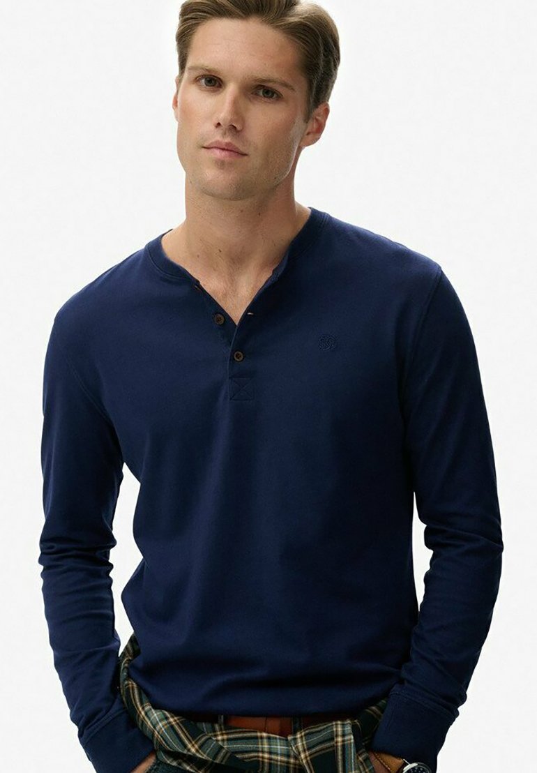 Marineblauwe henley-shirt met lange mouwen en drie bruine knopen bij de kraag. Glad katoen met een slim fit en geborduurd logo op de borst.