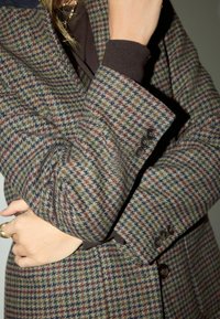 Wełniana marynarka w wzór houndstooth z brązowymi, zielonymi i burgundowymi odcieniami, z kontrastowymi ciemnymi wykończeniami mankietów oraz trzema guzikami na rękawie.