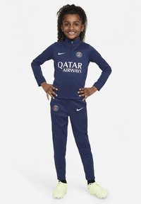 Marineblå træningsdragt med høj krave, med hvidt "Qatar Airways"-logo og Paris Saint-Germain-emblem. Bruges med knaldgule fodboldsko.