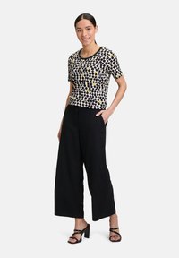 Haut à manches courtes avec un motif géométrique noir et crème, associé à un pantalon large taille haute noir et des talons noirs à lanières.