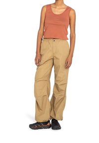 Pantalon cargo beige à coupe ample, taille élastique et multiples poches, associé à un haut sans manches couleur rouille et des chaussures de randonnée.