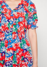 Vestido floral em vermelho, azul, verde e branco, com mangas curtas bufantes, decote em V e cintura franzida. Apresenta fecho com botões.