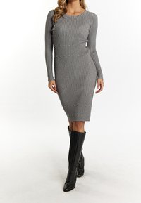 Graues Rippstrick-Kleid mit langen Ärmeln, verziert mit silbernen Nieten, figurbetonte Silhouette, kombiniert mit schwarzen kniehohen Lederstiefeln.