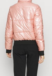 Rosa metallisk puffjacka med en kortad design, ribbade svarta mudd och fåll, samt kviltad yta. Jackan har en hög krage.