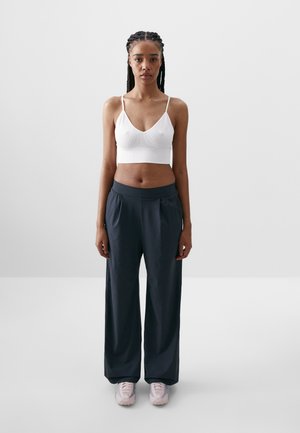 Hvit ribbet crop-top med tynne stropper, kombinert med løse, mørkegrå bukser med elastisk midje og sidelister. Lette joggesko.