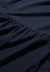 Tmavomodrá látka s na gathered ruffle detailom pozdĺž švu, ktorá vystihuje jemnú textúru a hladký povrch.