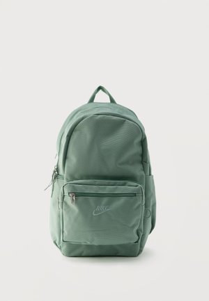 Rucsac Nike verde mentă, cu buzunar frontal cu fermoar, buzunare laterale și mâner superior, stând în picioare pe un fundal alb simplu.