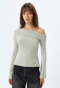 Lichtgrijze off-the-shoulder trui in een ribbelstructuur met lange mouwen, gecombineerd met donkergrijze denim. Eenvoudig, modern ontwerp.